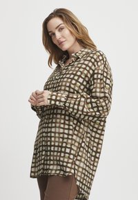 Chemise à carreaux marron avec des accents vert clair, manches longues, col à boutons et coupe décontractée, présentant un design à ourlet haut-bas.