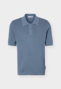 Ανοιχτό μπλε πλεκτό πόλο με κοντά μανίκια, υφασμένο σχέδιο, τρία κουμπιά και κλασικό γιακά, απεικονίζεται σε λευκό φόντο.