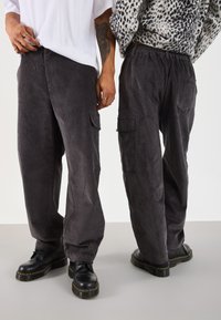 Two people wearing dark gray corduroy cargo pants and black boots, one facing front with white shirt, the other back with animal print sweater.