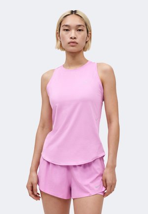 Jeune personne portant un débardeur de sport rose clair et un short assorti, debout devant un fond clair uni.