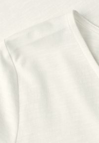 Gros plan d’un vêtement en coton blanc montrant la couture de l’épaule et la couture encolure en V avec une texture douce et un tissage uniforme du tissu.