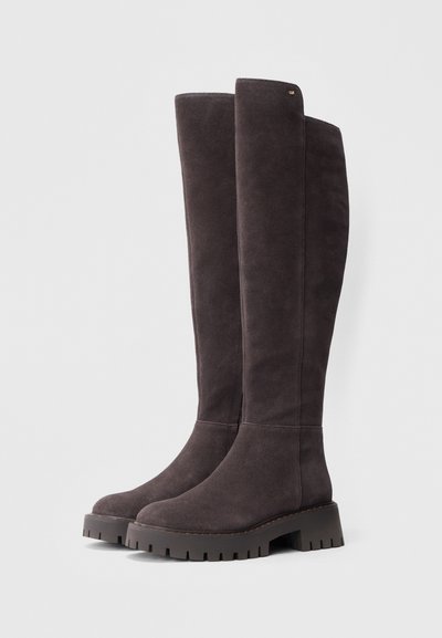 Bottes en daim gris foncé montant jusqu'au genou, avec une semelle plate et robuste ainsi qu'une légère plateforme ; elles présentent des coutures minimales et un petit logo en accent.