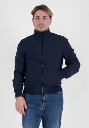 Giacca bomber navy realizzata in tessuto morbido, con colletto alto, zip frontale e polsini e orlo a coste. Dettaglio del logo ben visibile sul petto.