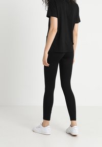 Camiseta negra de manga corta combinada con leggings negros, hechos de material elástico, usados con zapatillas deportivas blancas.