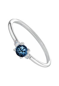 Anillo de plata con una piedra redonda azul central, flanqueada por dos piedras claras más pequeñas, y con una banda lisa y pulida.