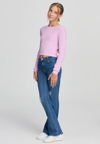 Jasnofioletowy prążkowany krótki sweter w zestawieniu z niebieskimi spódnicami dzwonami z postrzępionymi detalami, uzupełniony białymi trampkami.