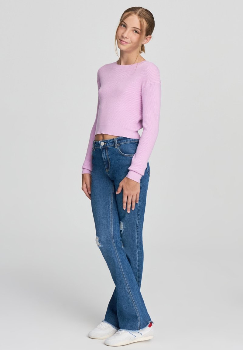 Jasnofioletowy prążkowany krótki sweter w zestawieniu z niebieskimi spódnicami dzwonami z postrzępionymi detalami, uzupełniony białymi trampkami.