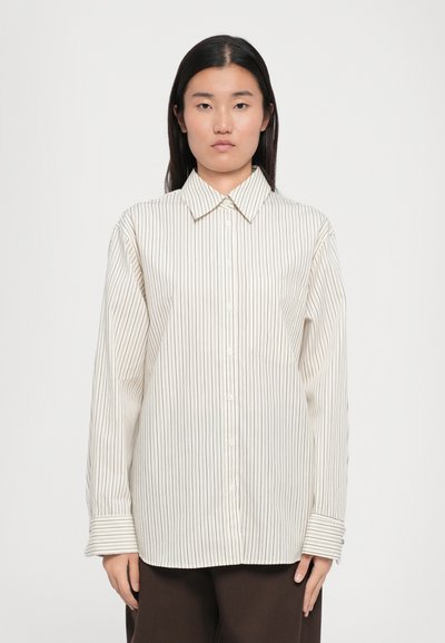 Camisa de manga larga a rayas en color crema con finas rayas verticales. Presenta un cuello clásico, botones en el frente y un bolsillo en el pecho.