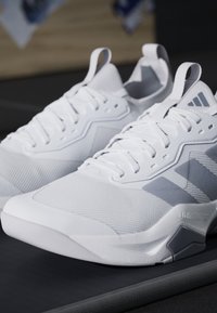 Coppia di scarpe da ginnastica bianche con dettagli grigi e linguette, che mostrano una trama dettagliata e il logo Adidas sulla linguetta e sul lato.