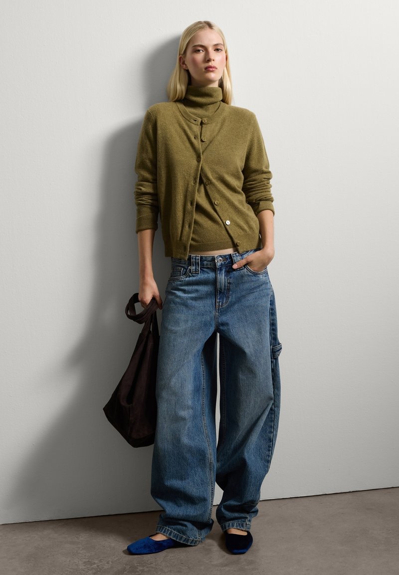 Cardigan en maille vert olive avec col roulé et boutons, associé à un jean en denim large bleu clair et un sac à bandoulière marron foncé.