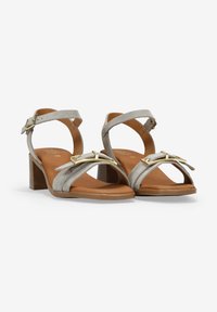 Sandalias de tacón bloque de gamuza gris con plantilla marrón, que cuentan con tiras cruzadas y una hebilla decorativa en tono dorado.