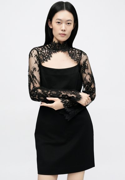 Svart kjole med tettsittende silhuett og firkantet halslinning, supplert med gjennomsiktige svarte blonder på lange ermer og krage.