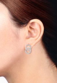 Boucles d'oreilles en argent présentant deux designs circulaires entrelacés, ornés de petites pierres claires. Surface lisse avec une finition polie.
