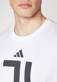 Hvid bomulds t-shirt med et fremtrædende sort grafisk design. Kraven er rund med en blød tekstur og minimal syning.