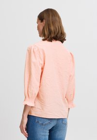 Peach short-sleeve blouse with a textured fabric, featuring a round neckline, elasticized puff sleeves, and a relaxed fit at the back.