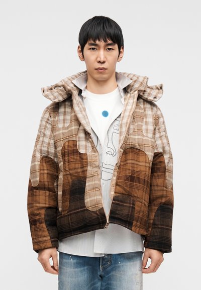 Καφέ και μπεζ καρό μπουφάν με κουκούλα, με κουτί σχήματος και αντιθετικές τσέπες. Φορεμένο πάνω από λευκό πουκάμισο και τζιν με φθορές.