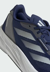 Scarpa da corsa blu navy con tomaia in rete testurizzata, accenti sintetici grigi e strisce riflettenti argento. Presenta una suola imbottita etichettata "LIGHTSTRIKE".