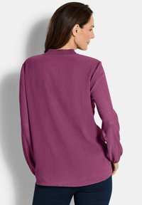 Langärmlige Bluse aus strukturiertem, tiefmagentafarbenem Stoff mit einem hohen Kragen und Raffung an den Bündchen.