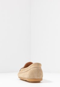 Beige semišové nazouvací boty s kulatou špičkou, nízkým profilem, texturovaným svrškem a gumovou podrážkou s mírným vzorkem.
