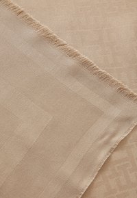 Beige sissekootud kangas kerge läikega, millel on tekstureeritud geomeetriline muster ja frantsiisitud serv ühelt poolt. Sile pind.