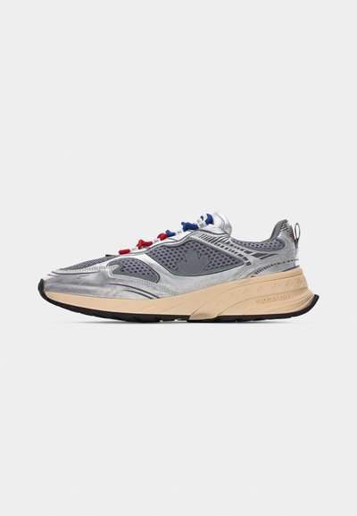 Baskets argentées et grises avec semelle beige, panneaux en mesh, et passants pour lacets rouges, blancs et bleus, présentées sur un fond clair uni.