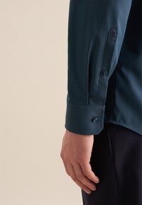 Donkerblauwe langemouwenshirt met een slanke pasvorm, met een manchetknoop met twee knopen en een geborduurd bloemenpatroon op de mouw. Glad stofoppervlak.