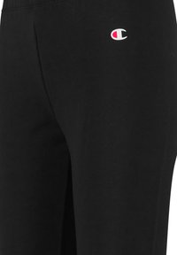Pantalones atléticos negros hechos de una mezcla de algodón, con un pequeño logotipo blanco y rojo en el muslo izquierdo. Textura suave, cinturilla elástica.