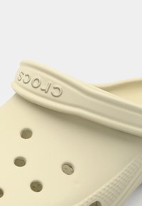 Sabots Crocs beiges en matériau léger ; dotés de trous de ventilation et d'une sangle de logo surélevée ; texture lisse avec des accents tactiles.