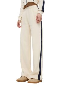 Pantaloni sportivi a gamba larga color crema con una striscia laterale blu navy, realizzati in tessuto morbido, dotati di vita elastica e vestibilità rilassata.