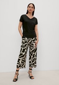 T-shirt nero a scollo a V abbinato a pantaloni larghi con un audace motivo astratto in bianco e nero, indossati con sandali neri con tacco.