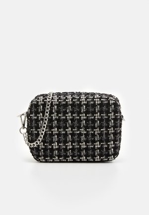 Pieni suorakaiteenmuotoinen mustavalkoinen tweed-laukku hopeisella ketjuhihnalla ja vetoketjusulkimella yksivärisellä taustalla.
