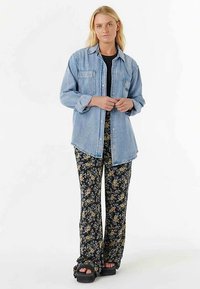 Jasnoniebieska jeansowa koszula z dwoma kieszeniami na piersi, zestawiona z czarnymi rozkloszowanymi spodniami w kwiaty i czarnymi sandałami na platformie.