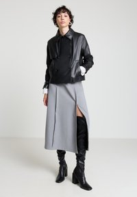 Schwarze, doppelseitige Lederjacke mit Kragen, kombiniert mit einem grauen Rock mit hohem Schlitz und kniehohen schwarzen Lederstiefeln.