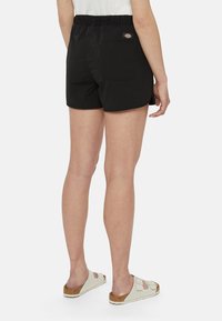 Pantaloni corti neri con vita elasticizzata, dotati di una tasca sul retro e di un piccolo patch con logo. Tessuto liscio e leggero con un taglio semplice.