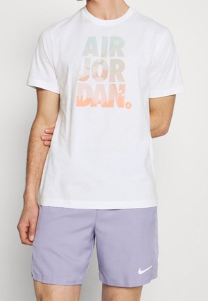 T-shirt en coton blanc arborant un graphique "AIR JORDAN" coloré dans des nuances pastel. Associé à un short violet clair et un logo Nike blanc.