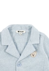 Camicia di cotone azzurro chiaro con colletto a pieghe, dotata di un'applicazione a forma di orso e chiusura a bottone. Comprende un'etichetta con dettagli del marchio e della taglia.