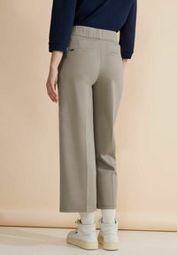 Ljusgrå vida byxor med en mjuk textur, som har hög midja, bakfickor och är parat med vita sneakers och strumpor.