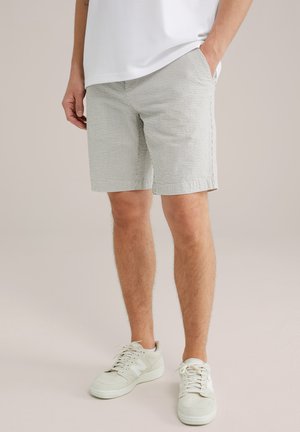 Lysgrønne stribede shorts med forlommer, parret med beige sneakers. Shortsene er knælange med lige snit og en struktureret stof.