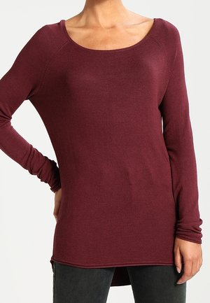 Top lungo color borgogna con scollo a barca, texture a costine e orlo leggermente curvo. Il materiale sembra morbido ed elastico.