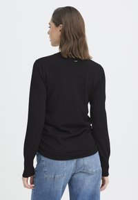 Czarny sweter z długim rękawem, okrągłym dekoltem i dopasowanymi mankietami, wykonany z miękkiego materiału. Z tyłu minimalistyczny wzór z małą metką.