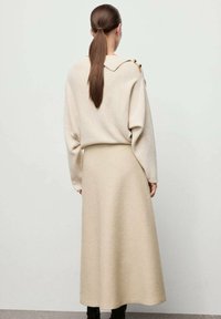 Suéter beige de gran tamaño con cuello y detalles de botones, combinado con una falda larga a juego. Textura suave, diseño minimalista.