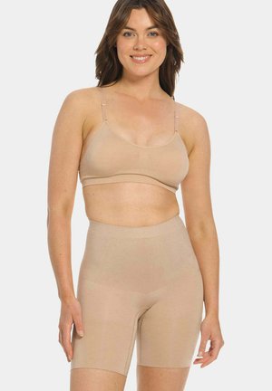 Woman wearing beige seamless high-waist shaping shorts and matching soft bra, standing and smiling against a plain white background.