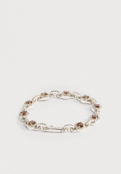 Ezüst karkötő összekapcsolt kör alakú foglalatokkal, mindegyikben barna drágakő látható, amelyet apró, tiszta kövek vesznek körbe, fehér háttéren.