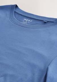 Niebieska t-shirt slim fit z okrągłym dekoltem, rozmiar średni, oznaczona "NEXT", położona na płasko na jasnej powierzchni.