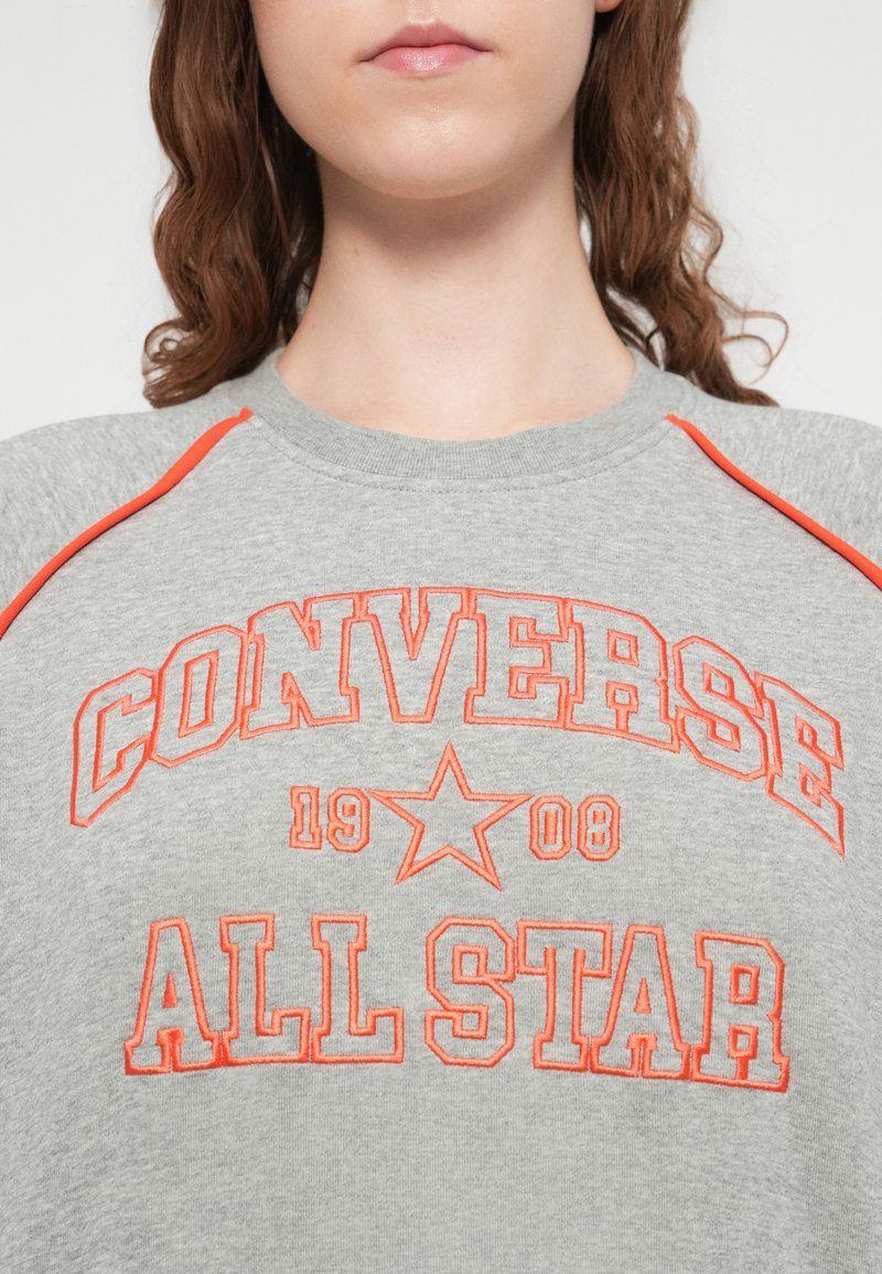 Grå sweatshirt med orange broderet tekst: "CONVERSE ALL STAR 1908." Ribstrikket rund halsudskæring og raglanærmer med orange detaljer.