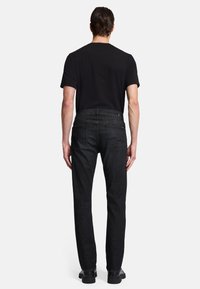 Zwarte denim jeans met een rechte pijp, voorzien van achterzakken en subtiele stikdetails, gecombineerd met een simpel zwart T-shirt.