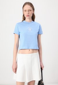 T-shirt cropped azzurro chiaro in cotone morbido con collo a giro. Abbinato a una gonna bianca a ruota, creando un outfit casual.