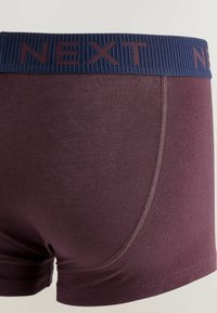Mörkröda boxershorts med en ribbad marinblå midja som har "NEXT" präglat i mörkröd. Slät textur och figurnära design, som framhäver sömdetaljerna.