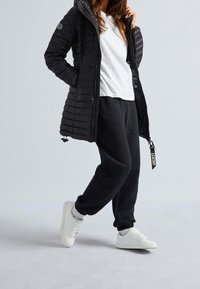 Svart puffjacka med huva, quiltat mönster och dragkedja. Matchas med svarta sweatpants och vita sneakers, som visar en avslappnad stil.