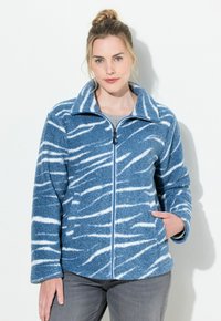 Niebieska kurtka polarowa z białym wzorem w zebry. Posiada zamek z przodu, stojący kołnierz i kieszenie po bokach. Miękka, teksturowana tkanina.